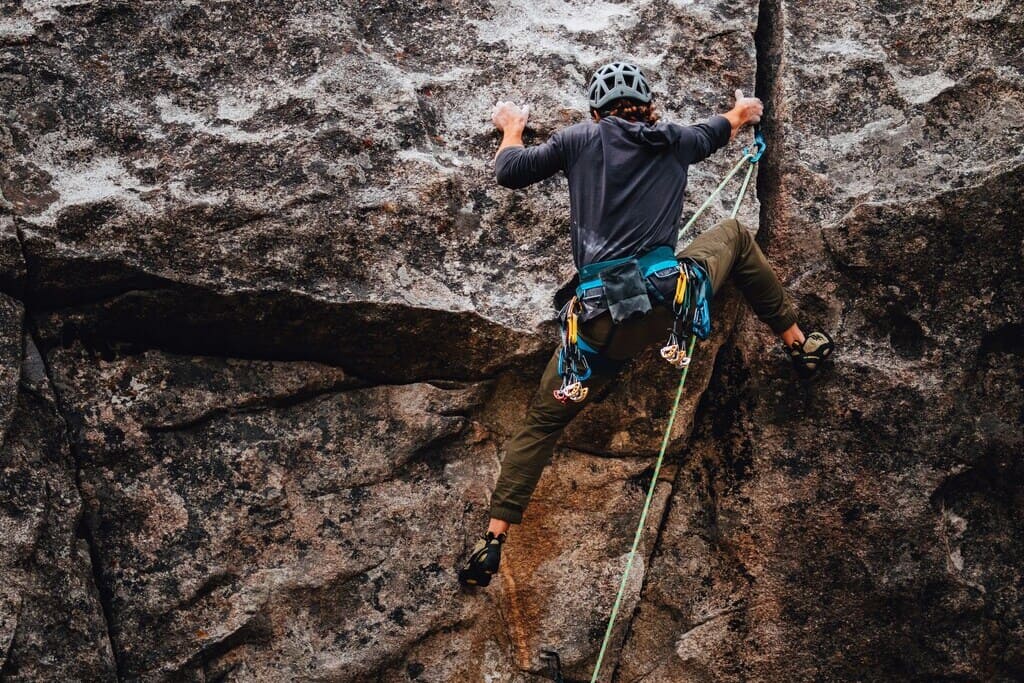 Kletterer am Fels mit funktionaler Kletterbekleidung Kletterer in Bewegung am Fels zeigt die Flexibilität und Funktion von moderner Kletterbekleidung