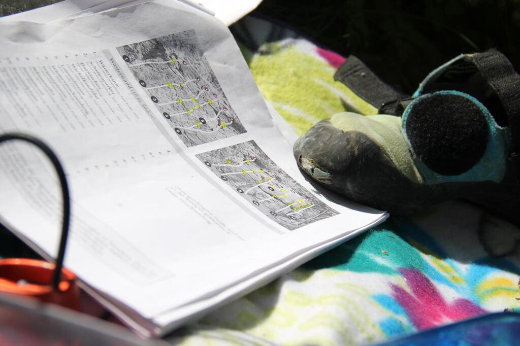 Kletter-Topo und Ausrüstung – Vorbereitung für die Wahl des Klettergebiets Ausgedrucktes Kletter-Topo liegt auf einer Decke neben einem Kletterschuh – Symbol für die Wahl und Planung eines Klettergebiets