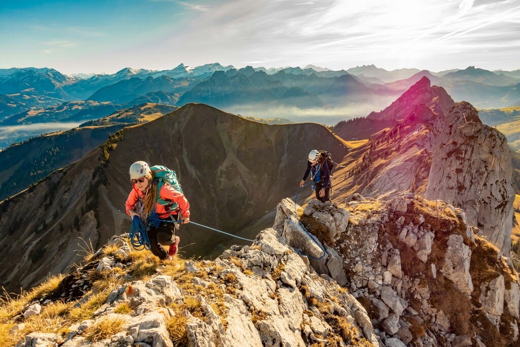 Outdoor Bekleidung beim Klettersteigen – Schutz und Funktion in alpinem Gelände Zwei Personen mit Outdoor Bekleidung beim Klettersteigen auf Bergkamm, aneinander gesichert, mit weitem Bergpanorama – zeigt Funktion und Schutz im Einsatz