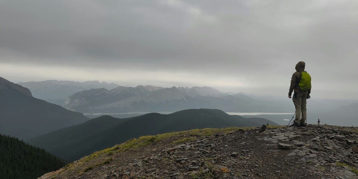 Wanderer auf einem Bergkamm mit weiter Aussicht, trägt wetterfeste Outdoor Bekleidung im Schichtenprinzip bei rauem Wetter